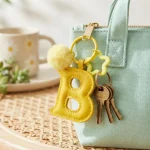Close-up of the letter pom pom keychain showing stitched yellow PU leather letter and faux fur pom pom.