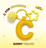Close-up of the Letter C keychain showing padded sunny yellow PU leather and soft faux fur pom pom.