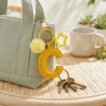 Close-up of the Letter C keychain showing padded sunny yellow PU leather and soft faux fur pom pom.
