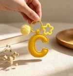 Close-up of the Letter C keychain showing padded sunny yellow PU leather and soft faux fur pom pom.