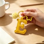 Close-up of the Letter E keychain showing padded sunny yellow PU leather and soft faux fur pom pom.