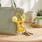 Close-up of the Letter E keychain showing padded sunny yellow PU leather and soft faux fur pom pom.