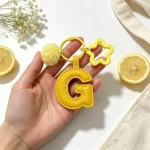 Close-up of the Letter G keychain showing padded gentle yellow PU leather and soft faux fur pom pom.