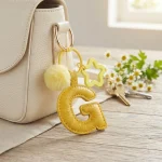Close-up of the Letter G keychain showing padded gentle yellow PU leather and soft faux fur pom pom.