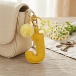 Close-up of the Letter J keychain showing padded jelly yellow PU leather and soft faux fur pom pom.