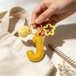 Close-up of the Letter J keychain showing padded jelly yellow PU leather and soft faux fur pom pom.