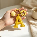 Close-up of the letter pom pom keychain showing stitched yellow PU leather letter and faux fur pom pom.