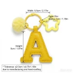 Close-up of the letter pom pom keychain showing stitched yellow PU leather letter and faux fur pom pom.