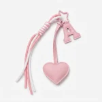 Personalized initial heart bag charm in pink PU leather with letter A and braided tassel on book flat lay